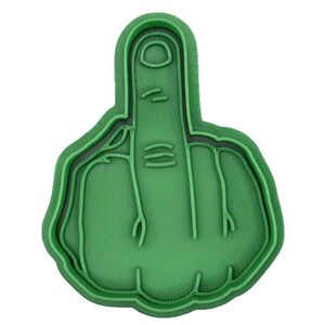 May include: A green plastic cookie cutter shaped like a hand giving the middle finger. The cutter has a detailed design with lines representing the finger's features and a layered outline.
