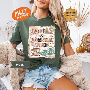 May include: A moss green t-shirt with the words "Coffee & Coastal Vibes" in a colorful design. The graphic includes a coffee cup, waves, and the word "Vibes". The shirt is part of a Comfort Colors collection.