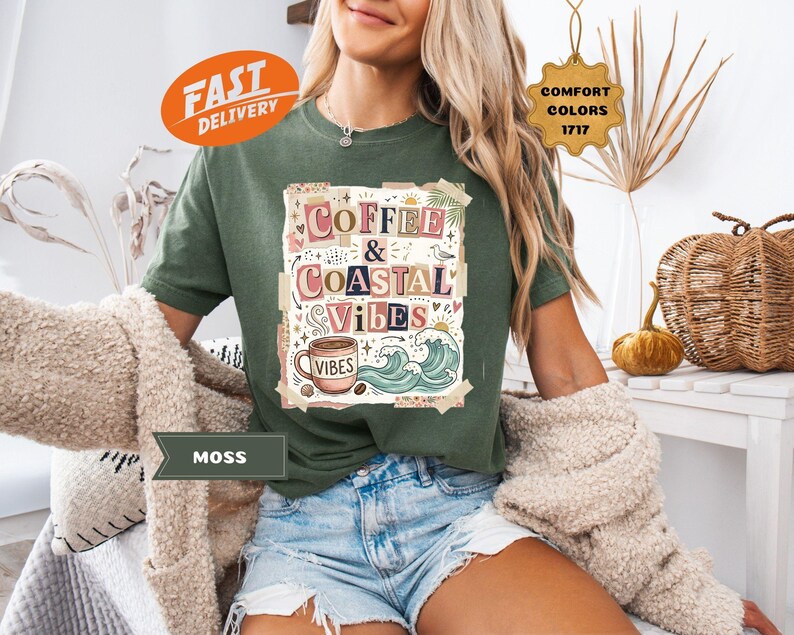 May include: A moss green t-shirt with the words "Coffee & Coastal Vibes" in a colorful design. The graphic includes a coffee cup, waves, and the word "Vibes". The shirt is part of a Comfort Colors collection.