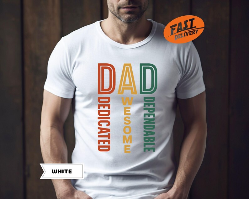 K&ouml;nnte beinhalten: Wei&szlig;es T-Shirt mit dem Wort "DAD" in Orange, "AWESOME" in Gelb und "DEPENDABLE" in Gr&uuml;n. Die W&ouml;rter "DEDICATED" sind vertikal in Orange ausgerichtet. Das Shirt hat auch einen "FAST DELIVERY" Aufkleber.