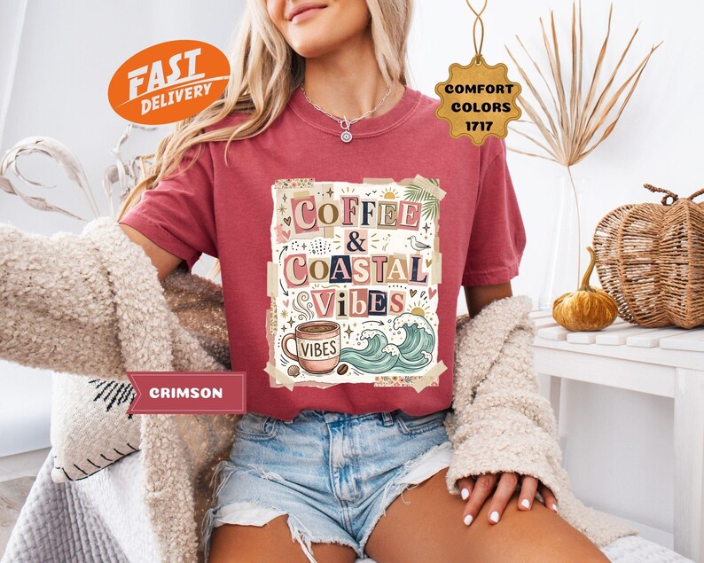 May include: Crimson-colored t-shirt with the words "Coffee & Coastal Vibes" in a decorative design. The shirt features a coffee cup, waves, and palm leaves. The shirt is paired with denim shorts.