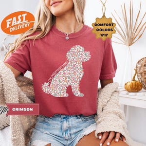May include: A red t-shirt with a floral doodle dog design and the text "Goldendoodle Mom". The shirt is being modeled by a person wearing denim shorts.