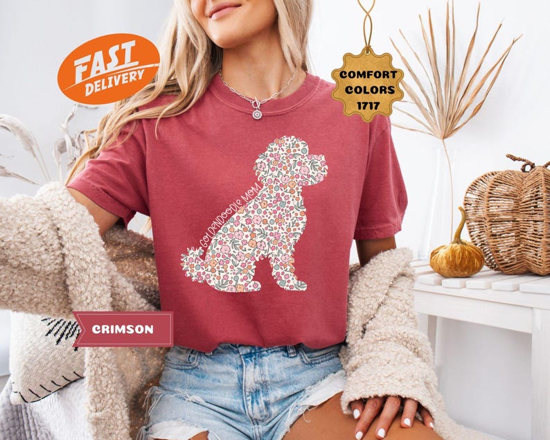 May include: A red t-shirt with a floral doodle dog design and the text "Goldendoodle Mom". The shirt is being modeled by a person wearing denim shorts.