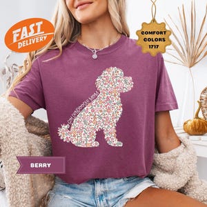 May include: A purple t-shirt with a floral doodle of a Goldendoodle dog. The text "Goldendoodle Mom" is written on the shirt.