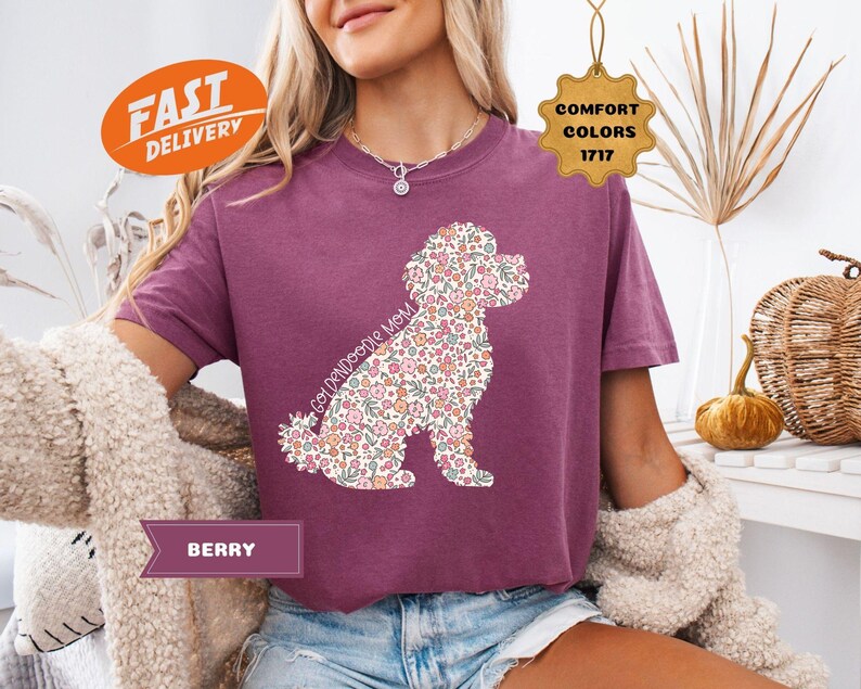 May include: A purple t-shirt with a floral doodle of a Goldendoodle dog. The text "Goldendoodle Mom" is written on the shirt.