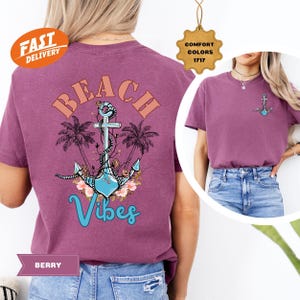 K&ouml;nnte beinhalten: Beerenfarbenes T-Shirt mit Strandmotiv. Das Design zeigt einen Anker, Palmen und die Worte "Beach Vibes" in einem stilisierten Schriftzug. Ein kleineres Anker-Motiv befindet sich auf der Vorderseite. Das Shirt ist ein Comfort Colors 1717.