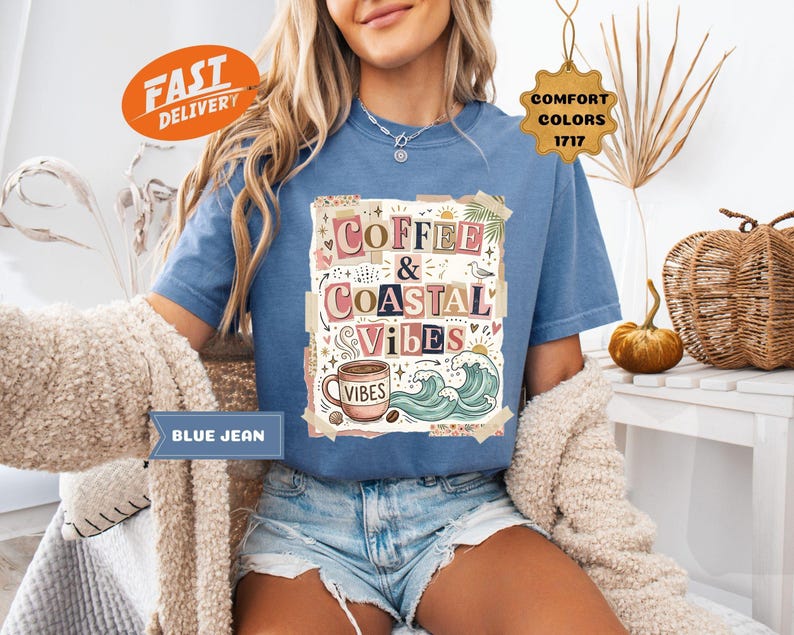 May include: Blue jean colored t-shirt with the words "Coffee & Coastal Vibes" in a collage design. The graphic includes a coffee cup, waves, and other coastal elements. The shirt has short sleeves and a crew neck.