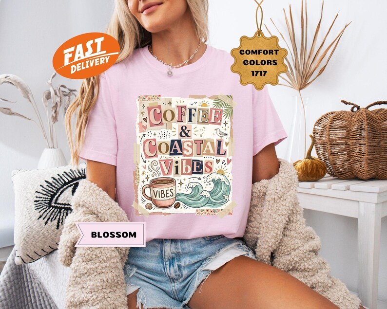 May include: A light pink t-shirt with the words "Coffee & Coastal Vibes" in a colorful, whimsical design. The graphic includes a coffee cup, waves, and other coastal elements. The shirt also has a "Fast Delivery" and "Comfort Colors" tag.