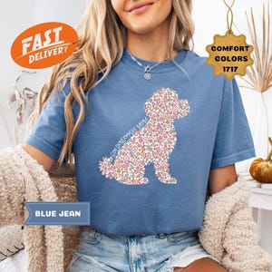 May include: A blue jean t-shirt with a floral poodle silhouette. The text "Golden Doodle Mom" is printed on the shirt.