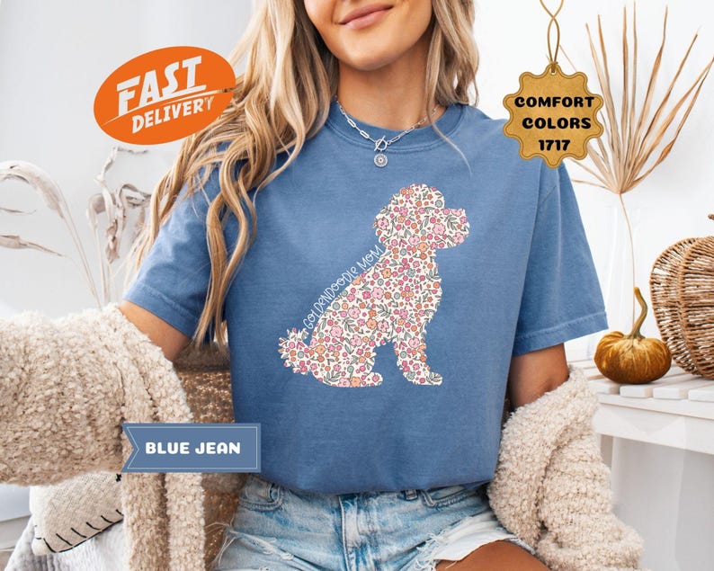 May include: A blue jean t-shirt with a floral poodle silhouette. The text "Golden Doodle Mom" is printed on the shirt.