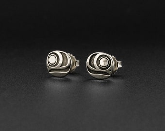 May include: A pair of silver earrings with a stylized design featuring a circle and a wave pattern.