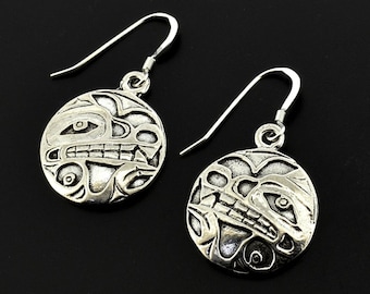 May include: A pair of silver earrings with a circular design featuring a stylised animal face. The earrings have a hook fastening.