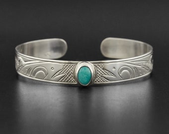 May include: Silver bracelet with a turquoise stone and an engraved design of two salmon.