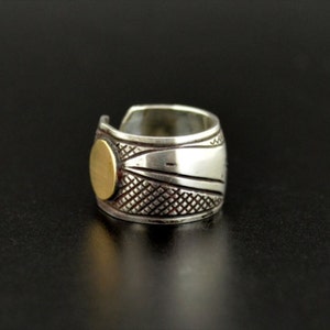 May include: Three silver rings with intricate designs. The ring on the left has a circular pattern, the middle ring has a geometric pattern with a gold circle, and the ring on the right has a similar geometric pattern with a gold circle.