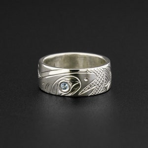 Può includere: Un anello d'argento con una scultura dettagliata di un uccello e una pietra preziosa blu nell'occhio. L'anello è largo e ha una finitura lucida.