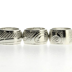 Könnte beinhalten: Drei silberne Ringe mit aufwendigen Designs. Die Ringe sind alle gleich groß und haben eine glatte, polierte Oberfläche.