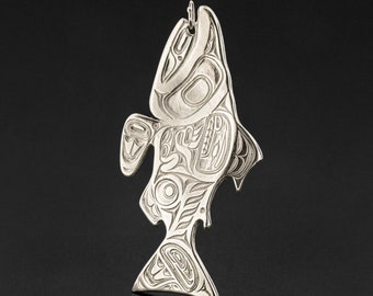 May include: A silver-colored pendant in the shape of a fish, featuring intricate engraved designs. The fish pendant has a loop at the top for a chain. The design is a stylized representation of a fish, with detailed patterns throughout its body.