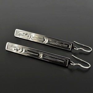 May include: A pair of silver dangle earrings with a detailed design of a stylized bird. The earrings are made of sterling silver and have a polished finish.