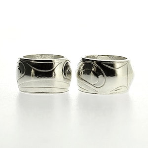 Könnte beinhalten: Zwei silberne Ringe mit einem geschnitzten Design. Die Ringe sind aus poliertem Silber gefertigt und haben ein detailliertes Muster.