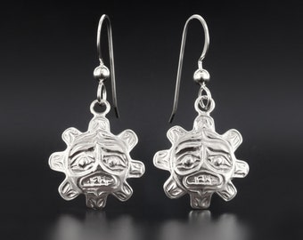 May include: A pair of silver dangle earrings featuring a stylized sun face design. The earrings are made of sterling silver and have a hook closure.