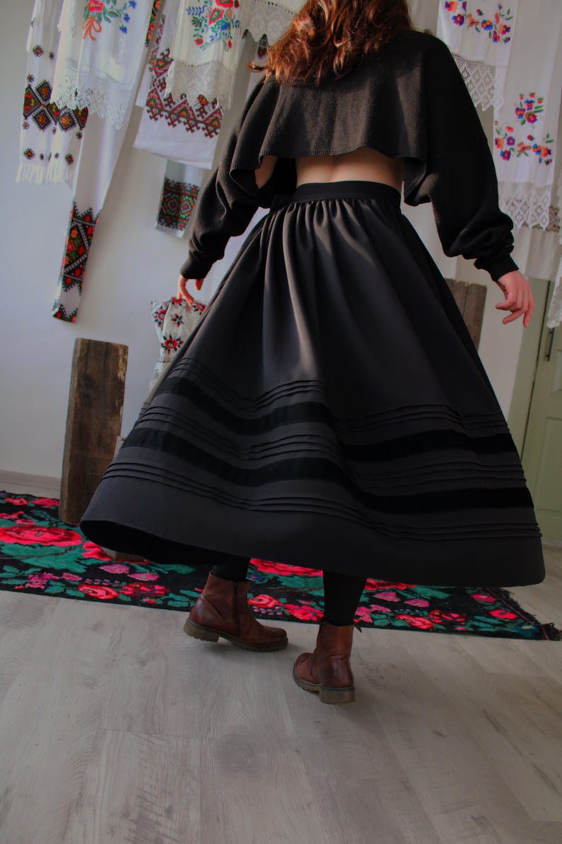 May include: A black skirt with three horizontal velvet bands, paired with a matching cropped top. The skirt is full and flowing. Handmade folk maxi skirt inspired by traditional European clothing, including Hungarian, Ukrainian, Romanian, Slovak, and Eastern European folk skirts. A versatile piece for boho maxi skirt looks, folk festival outfits, heritage-inspired fashion, slow fashion wardrobes, and handmade ethnic clothing.