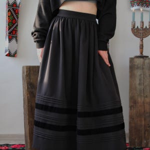 May include: A black skirt with pleated details and three horizontal velvet stripes near the hem. The skirt is paired with a black cropped sweater. handmade folk maxi skirt inspired by traditional European clothing, including Hungarian, Ukrainian, Romanian, Slovak, and Eastern European folk skirts. A versatile piece for boho maxi skirt looks, folk festival outfits, heritage-inspired fashion, slow fashion wardrobes, and handmade ethnic clothing.