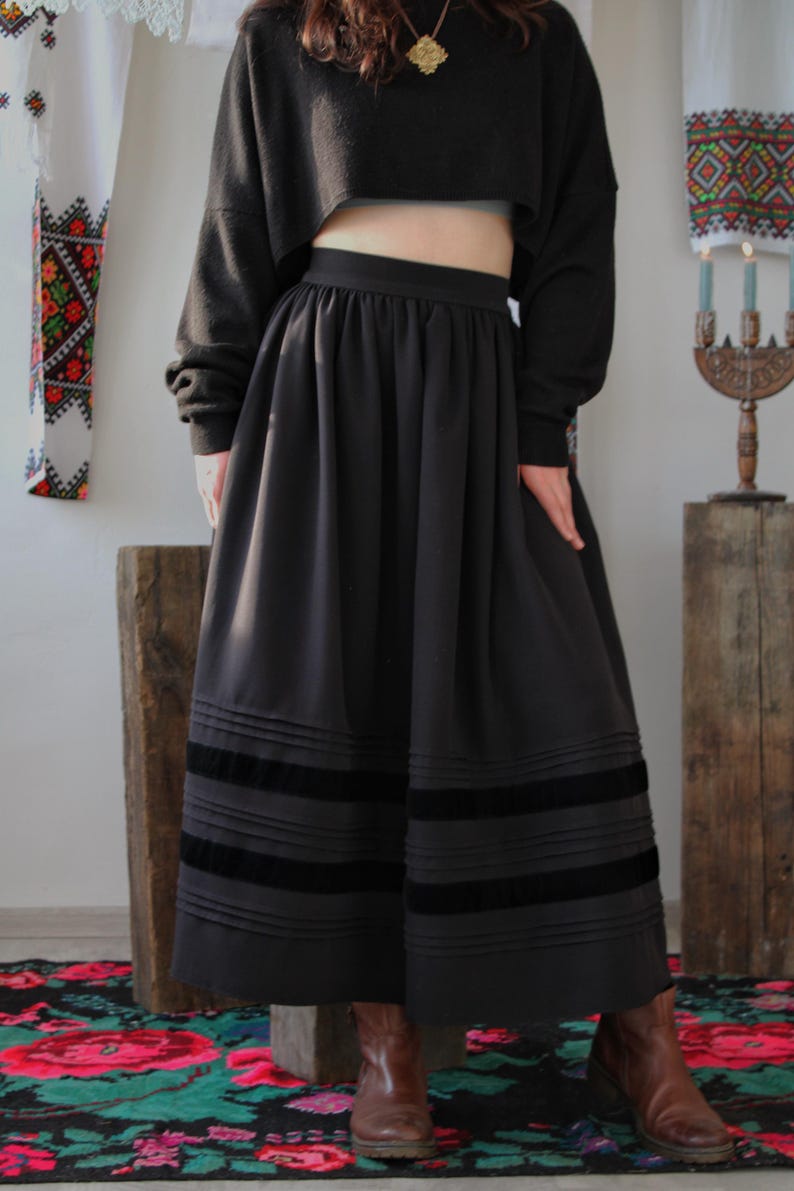 May include: A black skirt with pleated details and three horizontal velvet stripes near the hem. The skirt is paired with a black cropped sweater. handmade folk maxi skirt inspired by traditional European clothing, including Hungarian, Ukrainian, Romanian, Slovak, and Eastern European folk skirts. A versatile piece for boho maxi skirt looks, folk festival outfits, heritage-inspired fashion, slow fashion wardrobes, and handmade ethnic clothing.