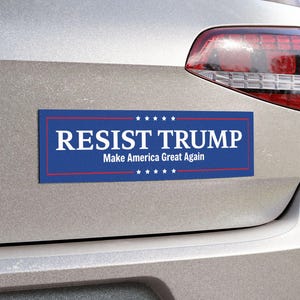Pode incluir: Adesivo azul para-choques com texto branco "RESIST TRUMP" e "Make America Great Again" abaixo. O adesivo retangular tem uma borda vermelha e estrelas brancas, fixado a um carro.