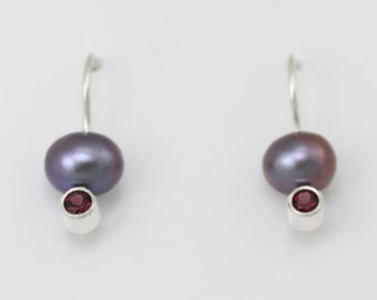 May include: A pair of silver earrings with a dark gray pearl and a small red gemstone on each earring.