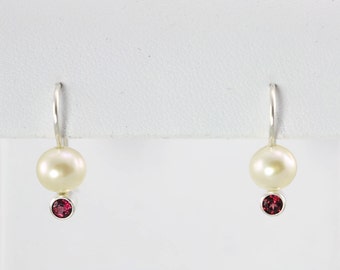 May include: A pair of silver earrings with a white pearl and a small red gemstone.