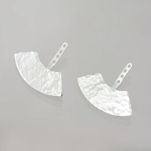 May include: A pair of silver earrings with a hammered, crescent moon shape. The earrings have a post and butterfly backing.