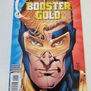 Może przedstawiać: Okładka komiksu "Convergence: Booster Gold #1". Okładka przedstawia podzielony obraz twarzy superbohatera z niebieskim i czerwonym tłem. Tytuł "BOOSTER GOLD" jest w złotych literach. Komiks jest oceniony jako T dla nastolatk&oacute;w.
