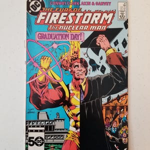 Może przedstawiać: Vintage okładka komiksu z Firestormem, Człowiekiem Nuklearnym, z napisem "GRADUATION DAY!". Grafika na okładce przedstawia podzielony obraz Firestorma w kostiumie superbohatera i mężczyzny w todze. Widoczne jest logo DC Comics.