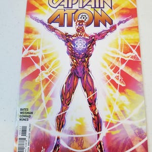 Może przedstawiać: Okładka komiksu "The Fall and Rise of Captain Atom" numer 4. Okładka przedstawia muskularną postać z świecącym symbolem atomu na piersi, z wyciągniętymi ramionami, otoczoną liniami energii. Tło to mieszanka pomarańczowego, ż&oacute;łtego i czerwonego.