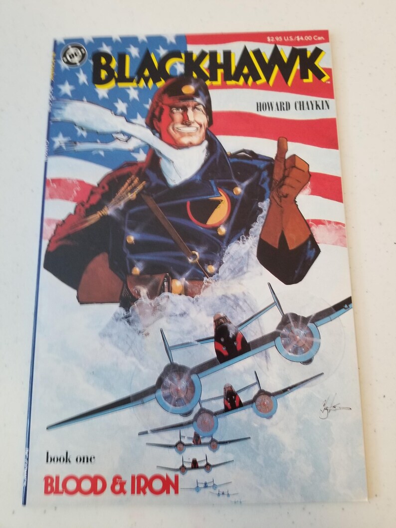 Może przedstawiać: Okładka komiksu w stylu vintage "Blackhawk" książka pierwsza, "Blood & Iron". Okładka przedstawia uśmiechniętego mężczyznę w mundurze wojskowym z uniesionym kciukiem, na tle amerykańskiej flagi i samolot&oacute;w bojowych.