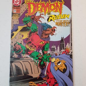 Może przedstawiać: Okładka komiksu "The Demon vs. Robin". Okładka przedstawia dynamiczną ilustrację dw&oacute;ch postaci w scenie walki, z żywymi kolorami i pogrubionymi literami. Komiks ma numer 23.