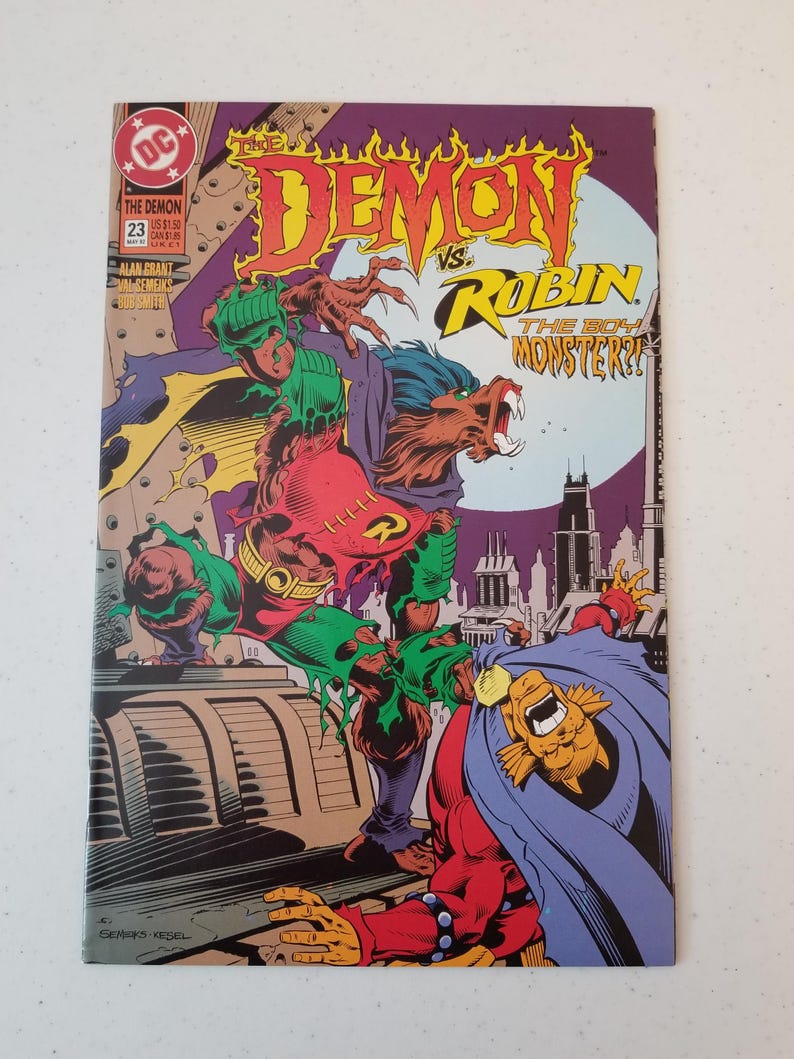 Może przedstawiać: Okładka komiksu "The Demon vs. Robin". Okładka przedstawia dynamiczną ilustrację dw&oacute;ch postaci w scenie walki, z żywymi kolorami i pogrubionymi literami. Komiks ma numer 23.