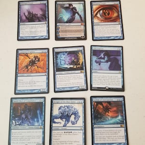 May include: Nine Magic: The Gathering trading cards are arranged in a 3x3 grid. The cards feature various creatures, spells, and enchantments with blue and orange color schemes. The cards include text and illustrations.