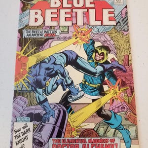 Może przedstawiać: Okładka komiksu z tytułem "BLUE BEETLE" w kolorze czerwonym. Grafika przedstawia dynamiczną scenę walki z Blue Beetle. Okładka zawiera tekst "THE ELEMENTAL MADNESS OF DOCTOR ALCHEMY!" i "How will THE DARK KNIGHT end?"