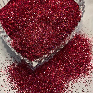 Puede incluir: Un cuenco de vidrio transparente en forma de corazón rebosante de purpurina roja vibrante. La purpurina se derrama sobre la superficie, creando un efecto brillante y texturizado. Ideal para manualidades y decoraciones.