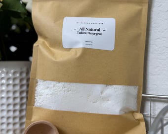 May include: A brown paper bag of All Natural Tallow Detergent with a clear window showing the white powder inside. A wooden measuring spoon with "1 Tbsp 15ml" is next to the bag. The label reads "All Natural Tallow Detergent".