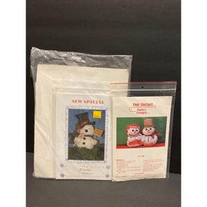 May include: A collection of snowman craft kits, including a "Sew Special" Frostie kit and a "The Snows" kit. The Frostie kit features a snowman illustration wearing a top hat. The Snows kit shows two snow people. The kits are packaged in clear plastic.
