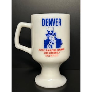 Może przedstawiać: Biały ceramiczny kubek z uchwytem, z napisem "DENVER" w niebieskich literach. Poniżej niebieska grafika wujka Sama wskazującego palcem, z tekstem: "DISTRICT RECRUITING COMMAND, USAR LIAISON NCO (303) 837-3322".