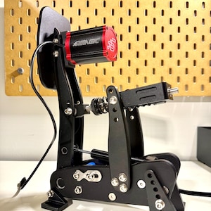 Può includere: Un set di pedali da corsa SIMAGIC neri e rossi. Il set presenta una base nera con pedali regolabili, un motore rosso e nero e vari componenti metallici. Il logo SIMAGIC è visibile sul motore.