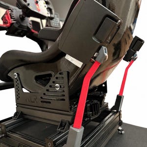 Könnte beinhalten: Schwarzer Rennsimulator-Sitz mit roten Sicherheitsgurten und Lenkrad. Der Sitz ist auf einem schwarzen Metallrahmen mit dem Text "NLR" und "FGT Lite" montiert. Das Lenkrad hat rote und gelbe Akzente.