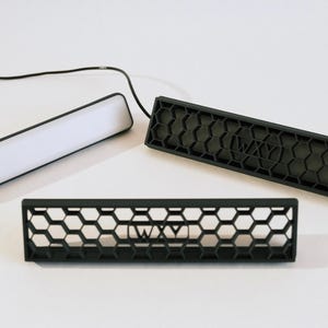 May include: Three black rectangular light fixtures are shown, featuring a honeycomb pattern and the text "WXY". One has a white light bar. All are presented on a white surface.