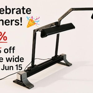 Peut inclure: Lampe de bureau noire réglable avec deux têtes d'éclairage. La lampe a une base rectangulaire et un bras flexible. L'image comprend le texte "Celebrate Fathers!" et "25%" avec un "20% de réduction sur tout le magasin jusqu'au 15 juin" barré.