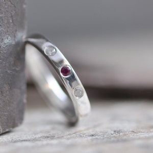 以下が含まれることがあります： 赤い宝石と2つの小さな白い宝石が付いた銀のバンドリング