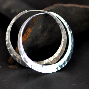 May include: A pair of silver hoop earrings with a hammered texture. The earrings are large and have a slightly oval shape.