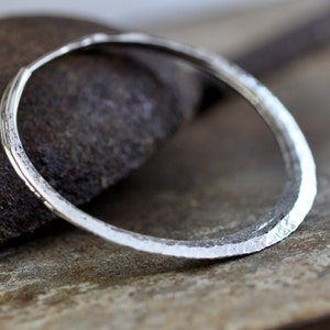May include: A silver hammered bangle bracelet with a smooth, rounded surface.